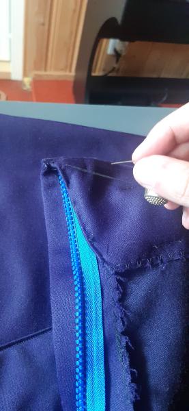 Couture à la main d'un des replis de la bande de taille, afin que celle-ci reste hors du chemin de la fermeture éclair autant que possible.